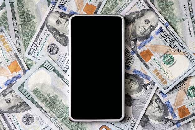 Large smartphone on money, close-up. Hundred dollar bill as a background. copy space. the concept of earning money through a smartphone or the Internet.