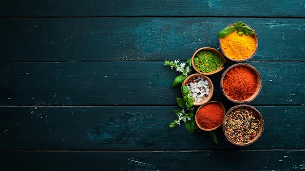 Large spice and herb collection in bowls and spoons. Indian spices. On a black wooden background. Top view.