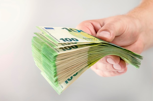 Large stack of euros in hand Banknotes of 100 euros in a male hand on a uniform background A man holds out his hand with a stack of banknotes as a concept of a loan insurance payment or mortgage