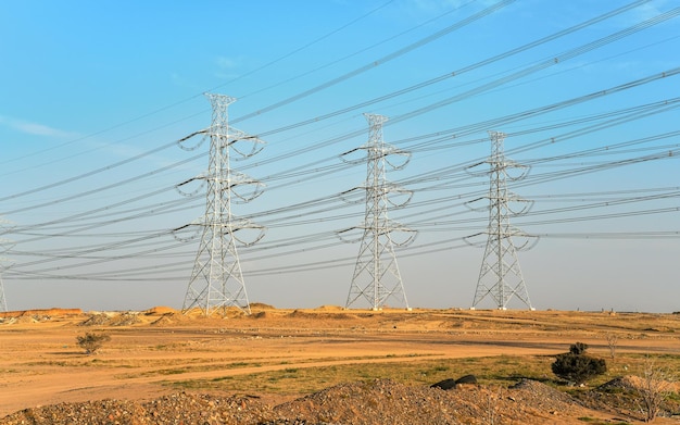 Large steel electricity power pylons with cables blue sky background afternoon sun shines on rather desert landscape around