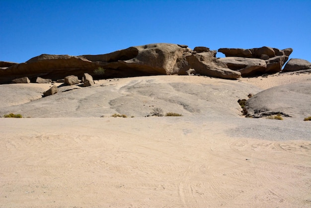 Large stone blocks lie on a desert hill Above them is a clear blue sky Arid surrounding natural