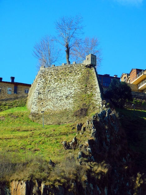 A large stone wall is on a hill in front of a house.