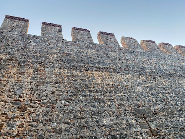 Large stone wall of an old ancient medieval fortress made of cobblestones against a blue sky