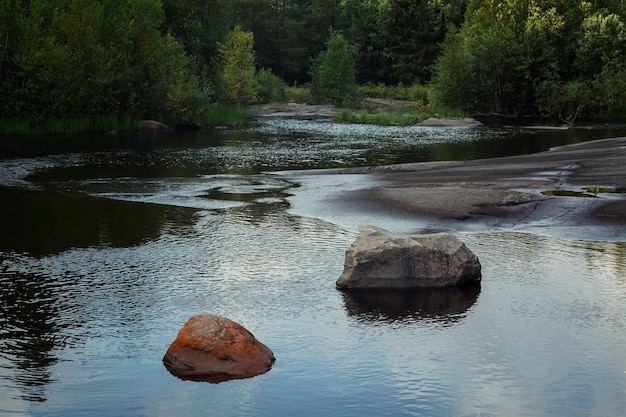 Large stones in a forest lake. Reflection of the sky with clouds in the water. Magnificent landscape.