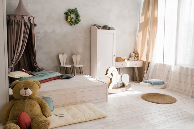 A large stuffed bear toy in the interior of a childrens room with a teepee Wooden horse gurney