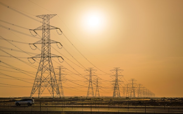 Foto grandi alti pilastri elettrici in acciaio in un paesaggio piuttosto piatto dell'arabia saudita solo silhouette nere visibili contro il sole luminoso del pomeriggio