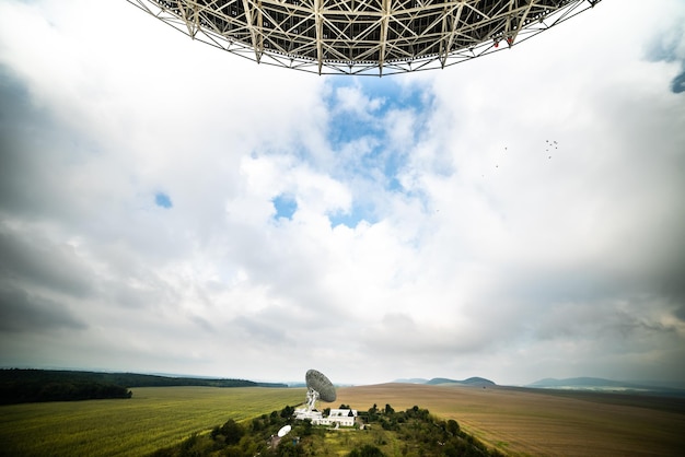 A large telescope is seen above a field of grass and a field with a blue sky.