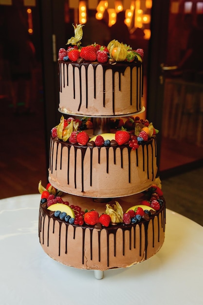 Большой трехъярусный свадебный торт на свадебном банкете, украшенный свежими фруктами и шоколадом Мягкий фокус