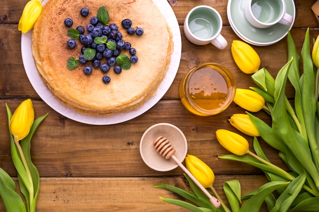 Foto grandi pancake russi tradizionali con bacche e miele su un tavolo di legno. cottura per le vacanze di primavera shrovetide e un mazzo di tulipani gialli. copia spazio.