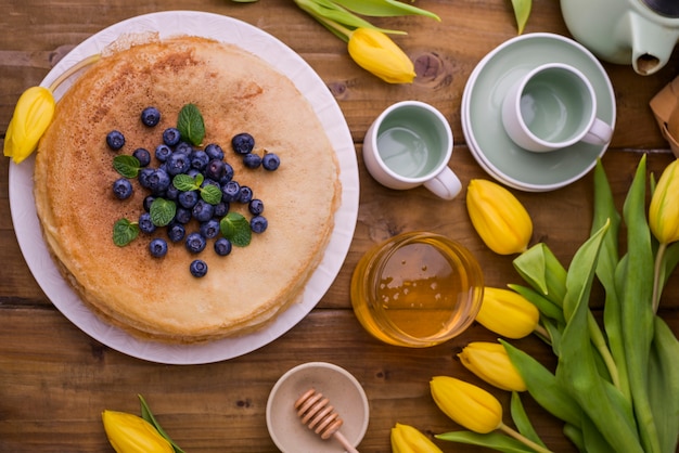 Foto grandi pancake russi tradizionali con bacche e miele su un tavolo di legno. cottura per le vacanze di primavera shrovetide e un mazzo di tulipani gialli. copia spazio.