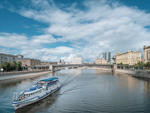 Photo large two-story white liner with tourists goes along moscow river. bridge over river in distance