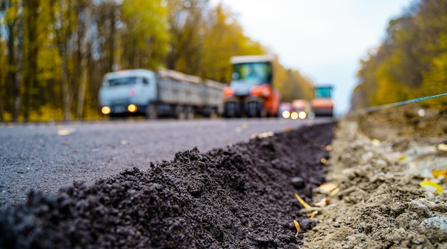 Large view on the road machinery working on the new road\
construction site fresh asphalt in front blurred machinery on\
background