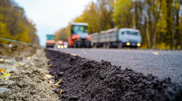 Large view on the road machinery working on the new road construction site. Fresh asphalt in front. Blurred machinery on background.