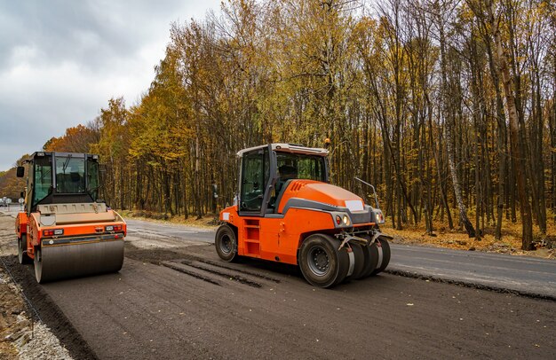 新しい道路建設現場で作業しているロードローラーの大きなビュー。道路の修復、クローズアップに選択的な焦点