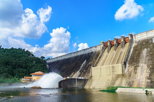 Стена плотины большого водохранилища выпускает воду с красивым небом