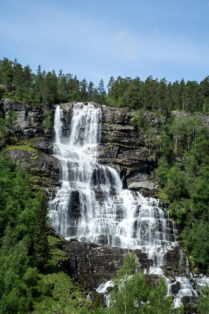 Large waterfall that rises in the mountains surrounded by green trees in Norway