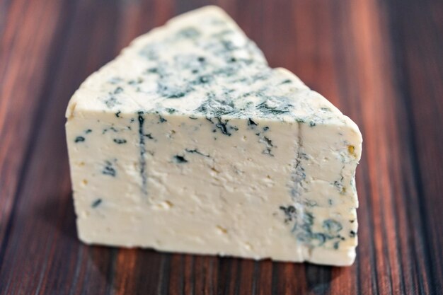 Large wedge of blue cheese on a dark wooden background.