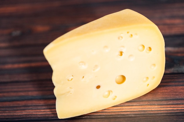 Large wedge of semi soft part-skim swiss cheese on a dark wooden background.