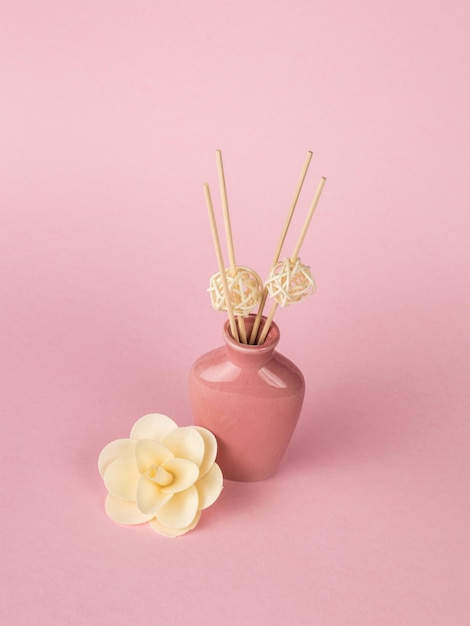 A large white flower and a pink vase with incense sticks on a pink background