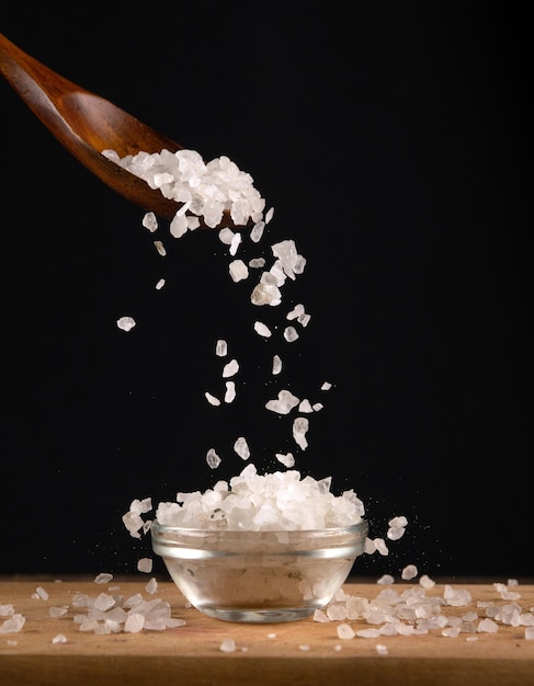 Large white salt is poured from a wooden spoon into a glass salt cellar