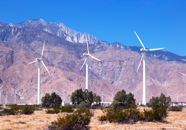 Large windmills in a clear blue sky against the backdrop of mountains and desert
