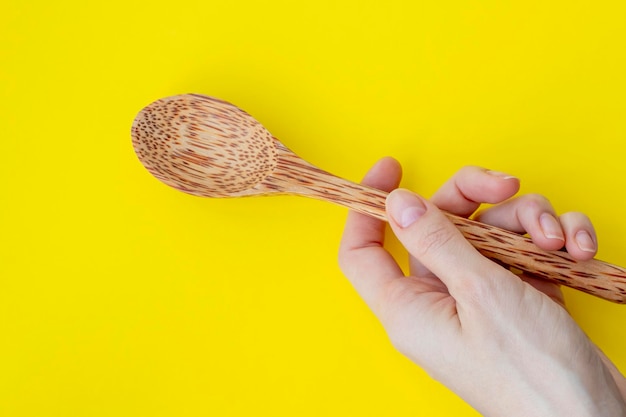 Large wooden spoon in a female hand on a bright yellow background