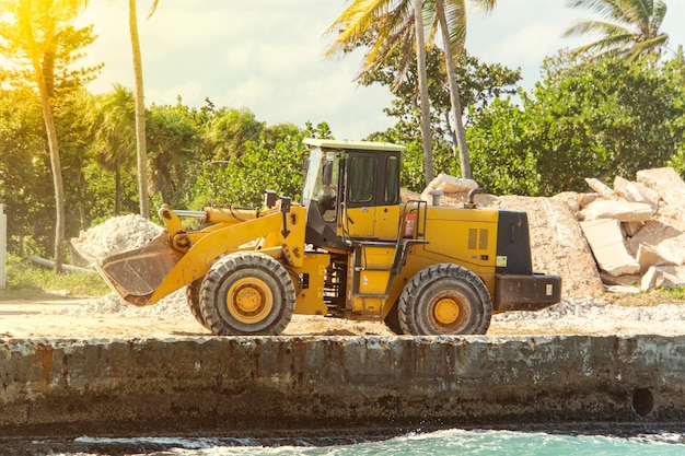 Large yellow bulldozer with jack hammer on construction site against background of palm trees construction of a hotel on island