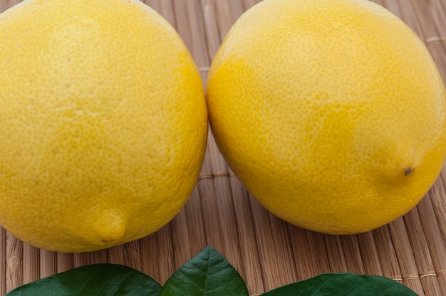 Large yellow lemons and green leaves close-up on bamboo mat.