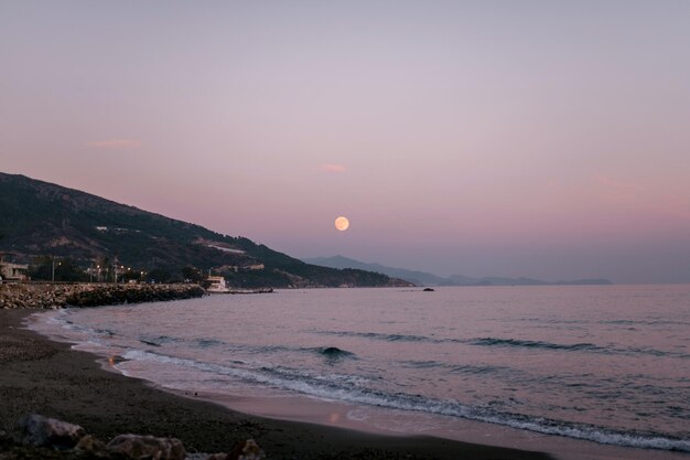 A large yellow sun is setting over the ocean.