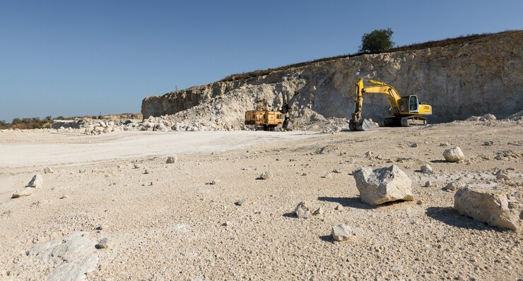 A large yellow tracked excavator is mining rock in a quarry.