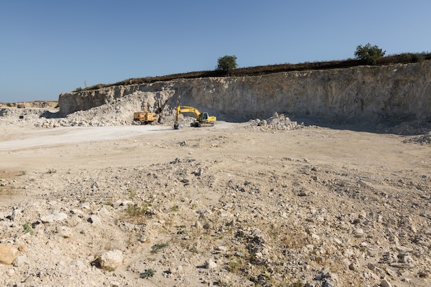 A large yellow tracked excavator is mining rock in a quarry.