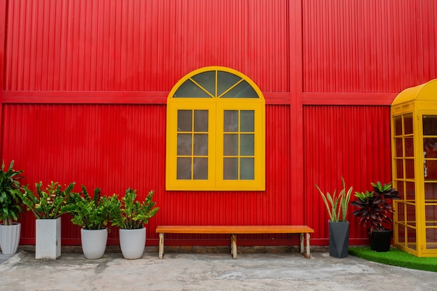 큰 노란색 창, 식물이있는 화분 및 도시 거리의 빨간 금속 벽에 벤치. 확대
