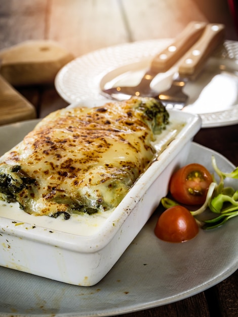 Lasagna in ceramic casserole dish served with tomato and herb, Italian food.