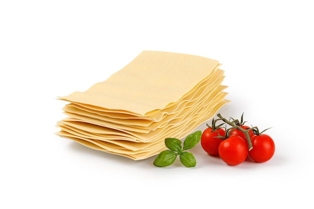 Lasagna sheets in stack with tomatoes and basil Uncooked lasagna pasta isolated on white background 