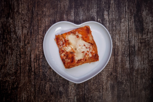 Lasagna with vegetables on dark wooden background. Traditional food health in white plate in form heart with Lasagna with vegetables. Delicious healthy food diet. Copy space