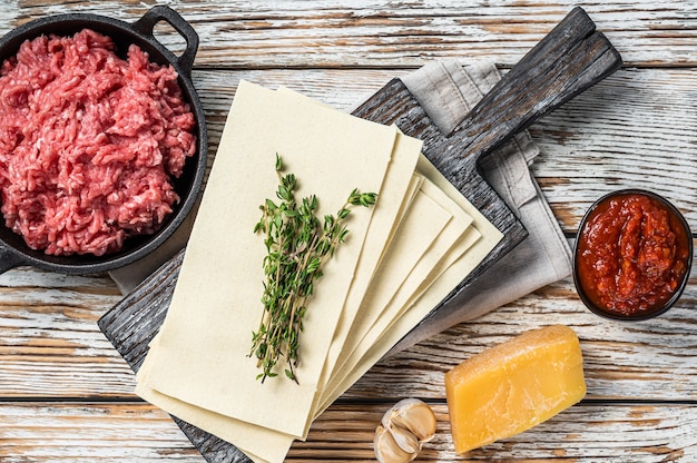 Lasagne rauwe vellen en andere ingrediënten. Witte houten achtergrond. Bovenaanzicht.