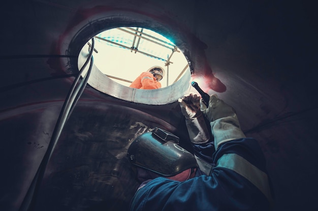 Lasboog argon werknemer man gerepareerd metaal is lasvonken industriële constructie tank onderdeel mangat roestvrij olie in besloten ruimtes er is een wachter buiten.