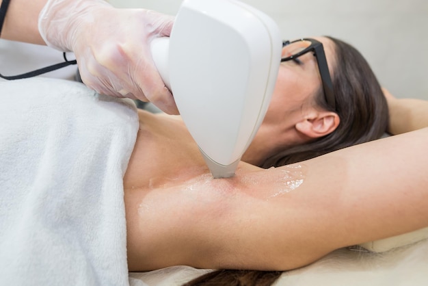 Foto depilazione laser e cosmetologia in un salone di bellezza procedura di depilazione il concetto di depilazione laser cosmetologia spa e depilazione bella donna bruna che ottiene la depilazione delle ascelle