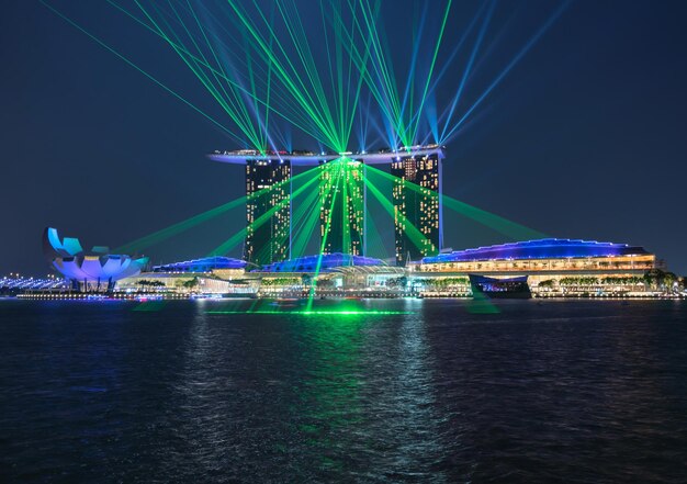 Laser light display on illuminated marina bay sands by sea at dusk