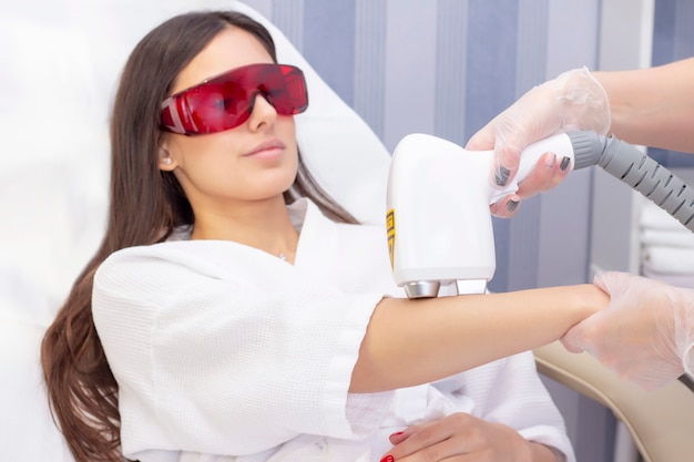 Laser ontharing en cosmetologie. de vrouw verwijdert haar op haar arm met een laser. cosmetologie ontharingsprocedure. laser ontharing en cosmetologie. cosmetologie en spa concept