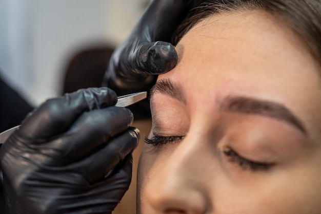 Lashmaker makes a beautiful eyebrow contour with tweezers female face closeup