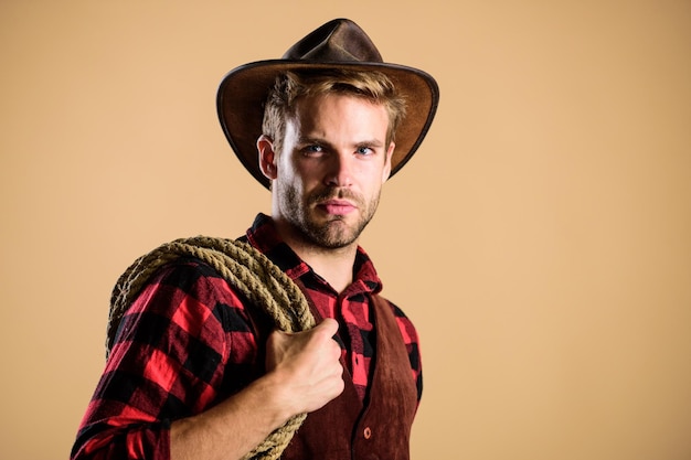 Lasso wordt gebruikt in rodeo's, deels competitieve evenementen. Lasso kan worden vastgebonden of verpakt. Westers leven Man cowboy beige achtergrond Man met hoed houdt touw vast Ranch beroepen Lasso gereedschap van Amerikaanse cowboy