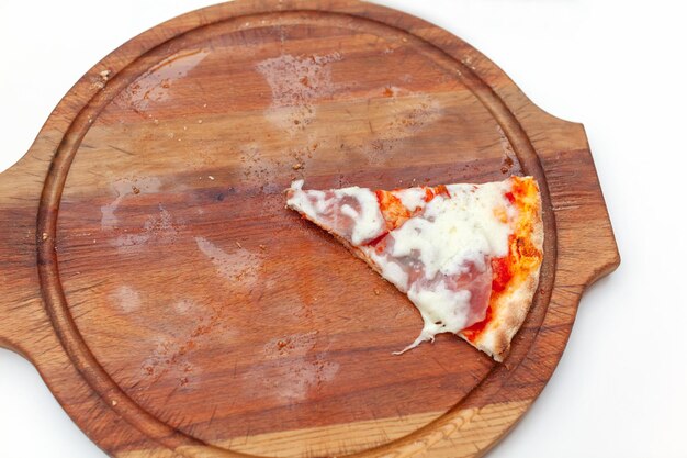 Last one slice of delicious italian pizza with ham and cheese on wooden board on white table