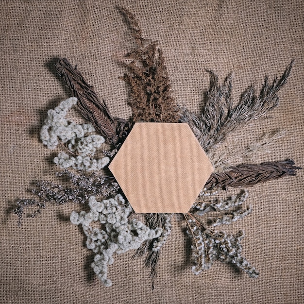 Lasting faded sustainable flowers with hexagonal frame on brown canvas background. Composition of dried flowers for Valentine's day, wedding or womans day on natural burlap. Square.