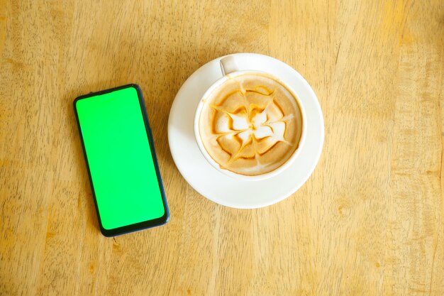 遅いコーヒーとテーブルの上に緑色のスクリーンが付いたスマートフォン