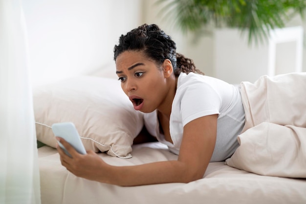 Photo late for work shocked overslept black woman looking at smartphone in hand