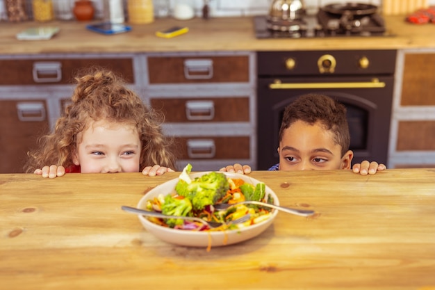 Laten we gaan spelen. Opgetogen brunette jongen leunend op tafel terwijl hij plezier heeft met zijn neef