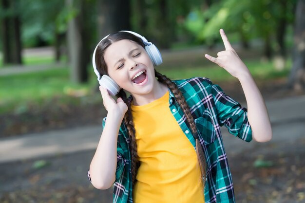 Laten we rocken. Gelukkig kind Toon hoorns handgebaar. Meezingen met muziek. Luister technologie. Moderne levensstijl. Mode uitstraling. Kinderdag. Zomervakantie. Rock-'n-roll-ziel.