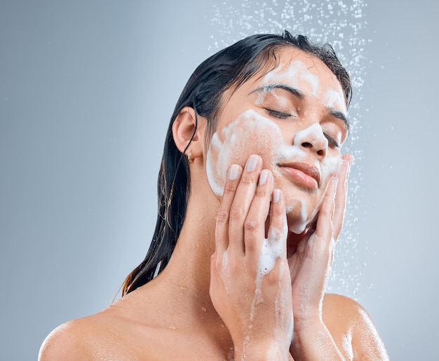 Lather it up Shot of a young woman washing her face in the shower against a grey background