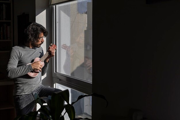 Foto latijns-amerikaanse man die ukelele speelt voor het raam